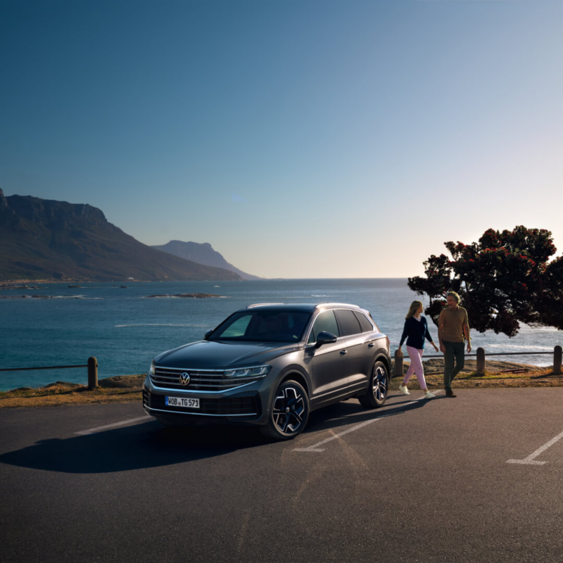 Una pareja junto a un Volkswagen Touareg aparcado frente al mar