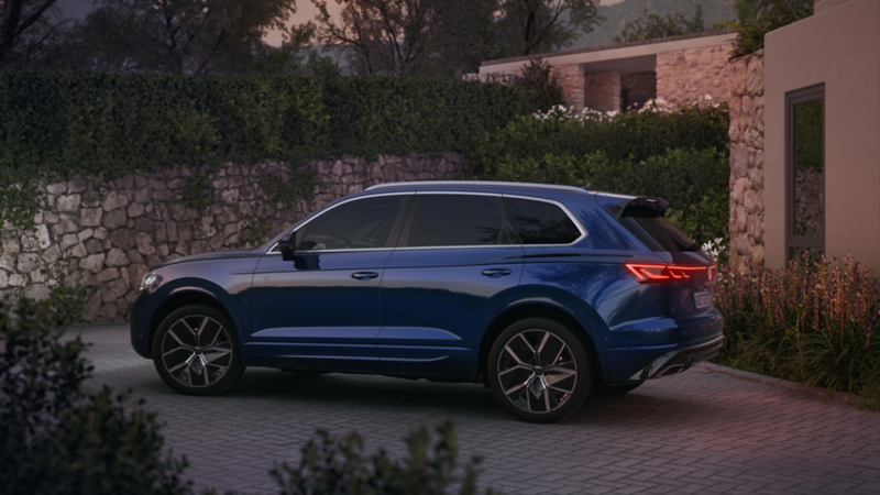 Un Volkswagen Touareg de color azul oscuro estacionado fuera de una casa
