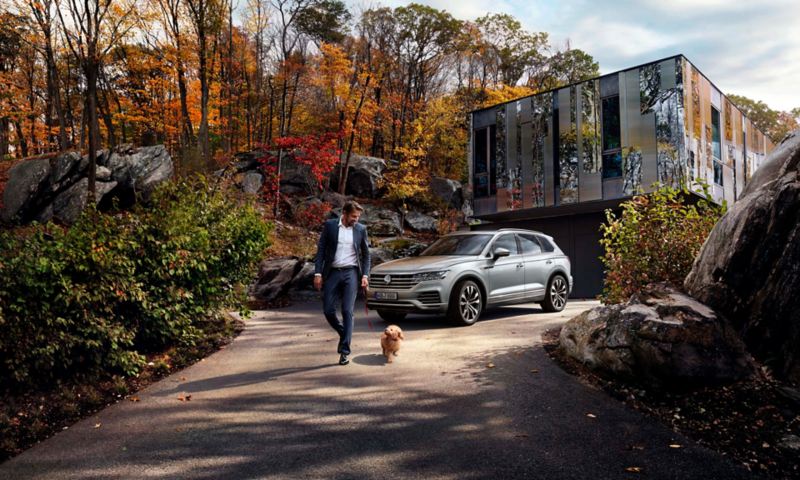 Hombre paseando un perro delante de un Volkswagen Touareg aparcado frente a una casa