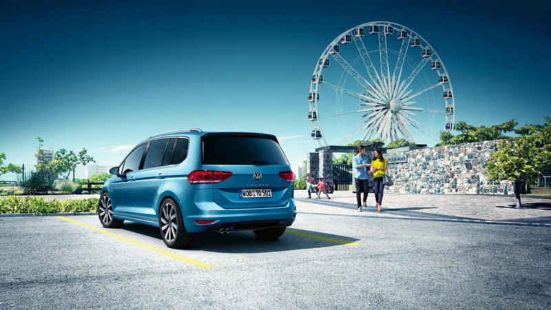 Un Volkswagen Touran visto desde la parte de atrás estacionado junto a un parque temático