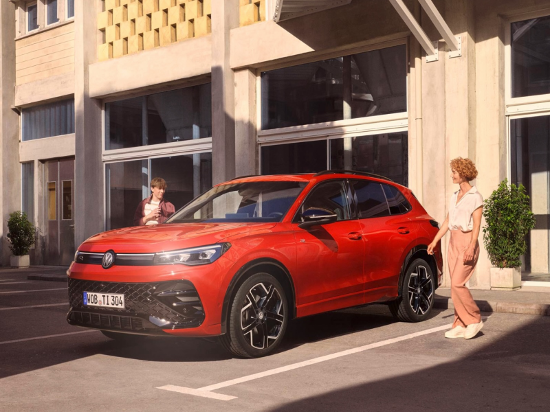 Un chico y una madre al lado de un Volkswagen Tiguan de color rojo estacionado en la calle