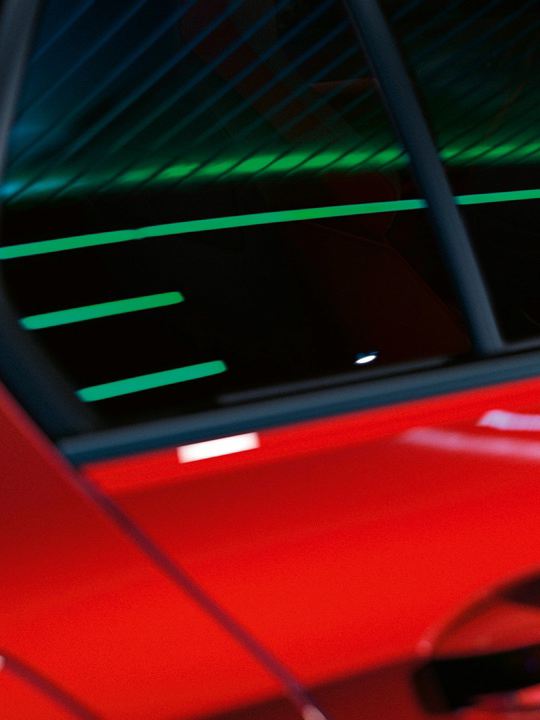 Detalle de la puerta trasera y la ventanilla de un Golf GTI rojo con reflejos de luces de neón