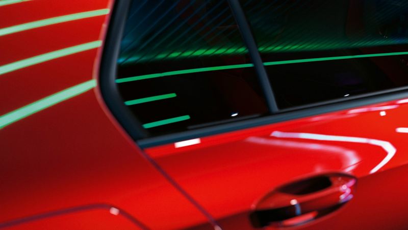 Detalle de la puerta trasera y la ventanilla de un Golf GTI rojo con reflejos de luces de neón