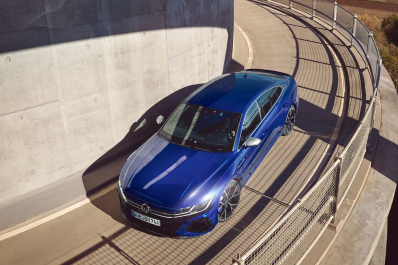 Vista superior de un Nuevo Volkswagen Arteon R azul bajando por una curva