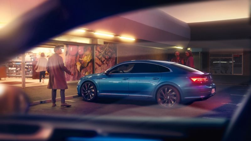Hombre junto a un Nuevo Volkswagen Arteon azul aparcado en la calle por la noche