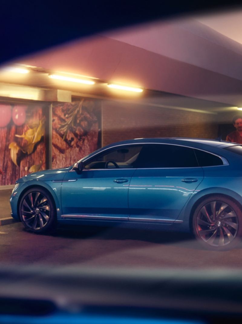 Hombre junto a un Nuevo Volkswagen Arteon azul aparcado en la calle por la noche
