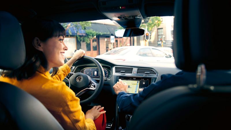 Chica sonriendo al volante de un Volkswagen vista desde el asiento de atrás