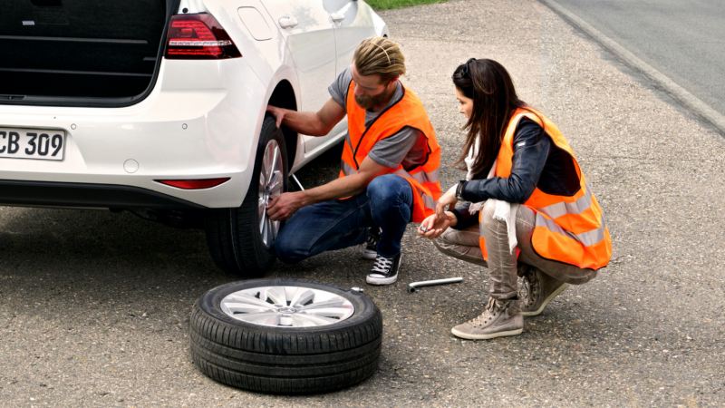 Un hombre y una mujer cambiando la rueda de un Volkswagen en el arcén de una carretera