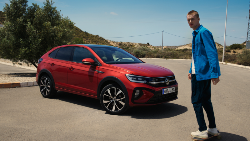 Chico delante de un Volkswagen Taigo rojo en una carretera