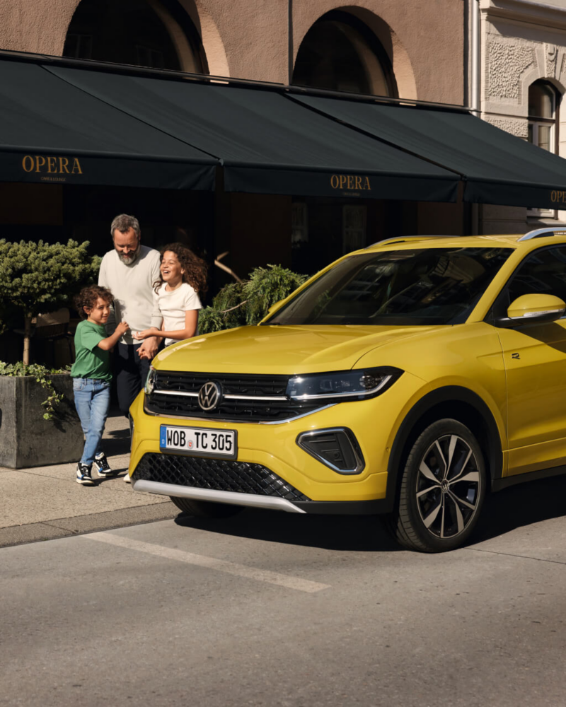 Una familia junto a un Volkswagen T-Cross de color amarillo estacionado en la calle