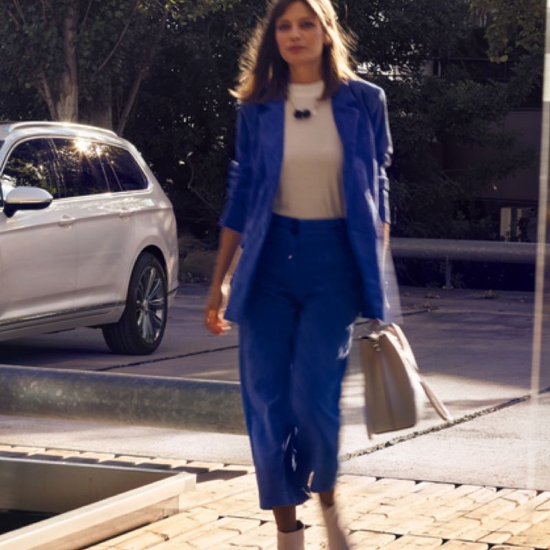 Mujer vestida de azul caminado y un Volkswagen Passat que se ve parcialmente al costado