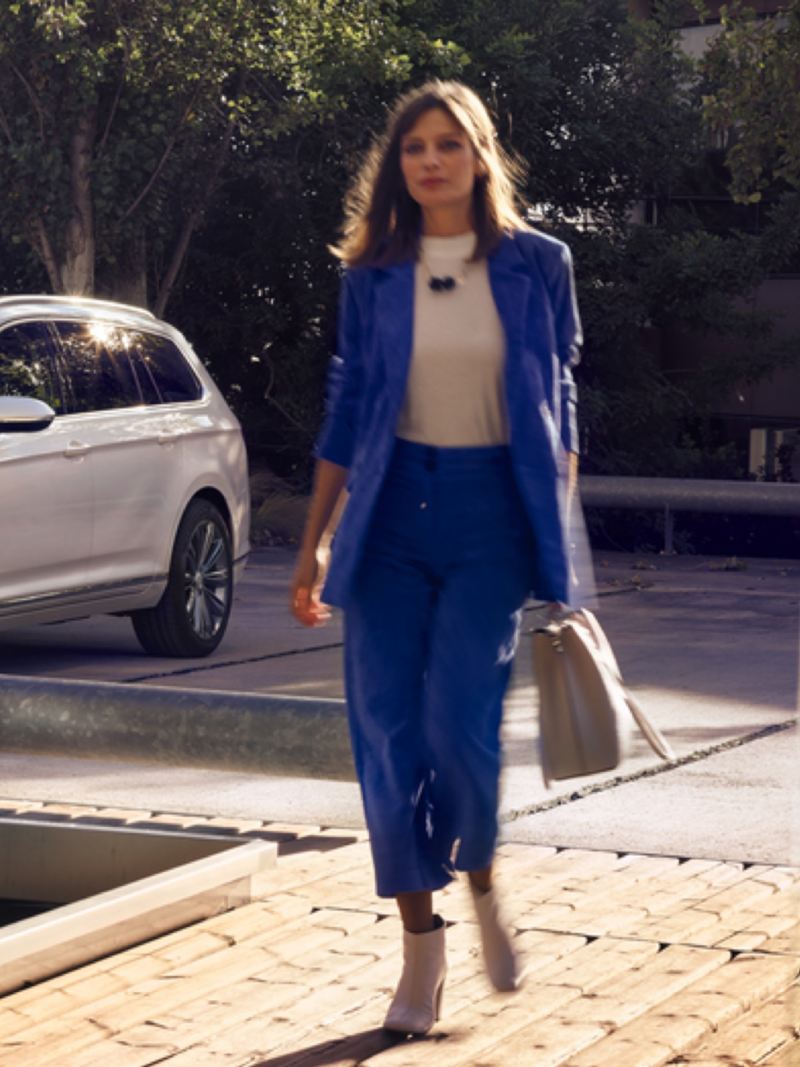 Mujer vestida de azul caminado y un Volkswagen Passat que se ve parcialmente al costado