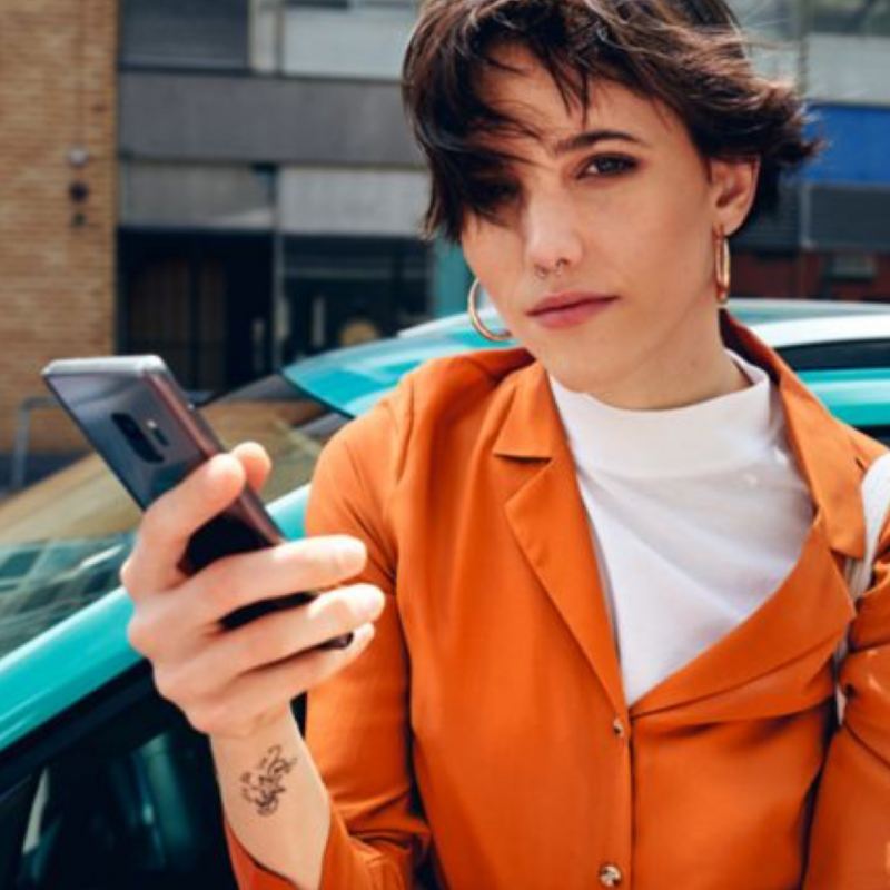 Chica vestida de naranja con un móvil en la mano mirando la cámara