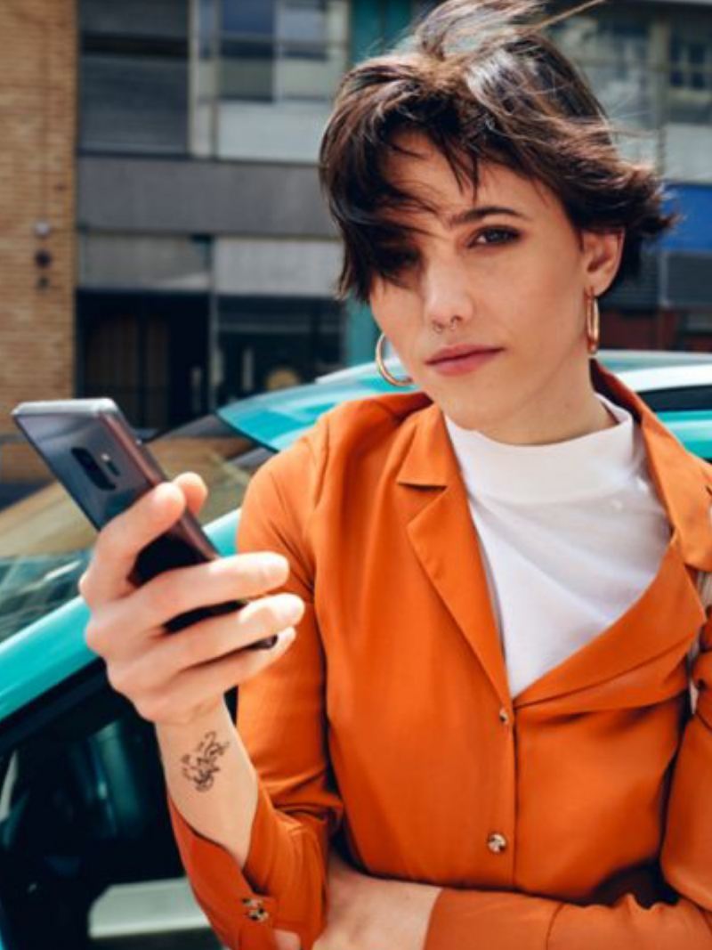 Chica vestida de naranja con un móvil en la mano mirando la cámara
