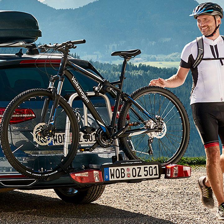 Ciclista de pie al lado de un coche con una bicicleta colocada en el porta bicicletas posterior