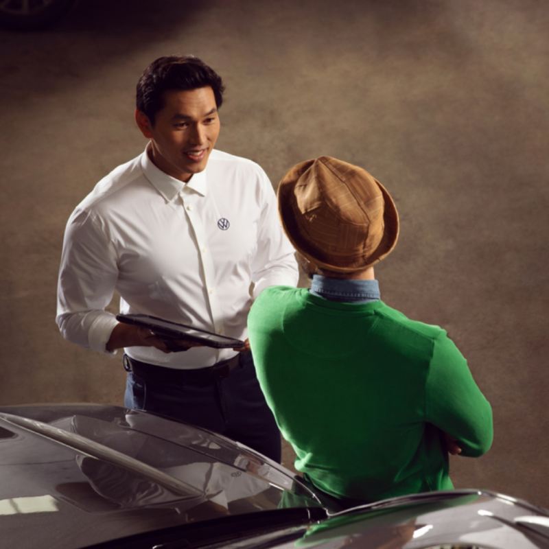 Dos hombres jóvenes hablando apoyados en el capó de un Volkswagen