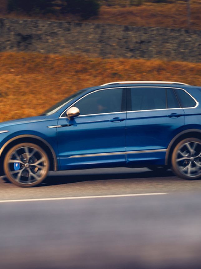 Vista lateral de un Volkswagen Tiguan azul avanzando por una carretera