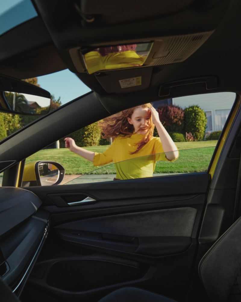 Niña pelirroja vestida de amarillo asomándose a un Volkswagen Golf 8 vista desde el interior