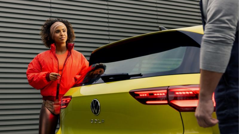 Chica hablando con un chico detrás de un Volkswagen Golf 8 amarillo