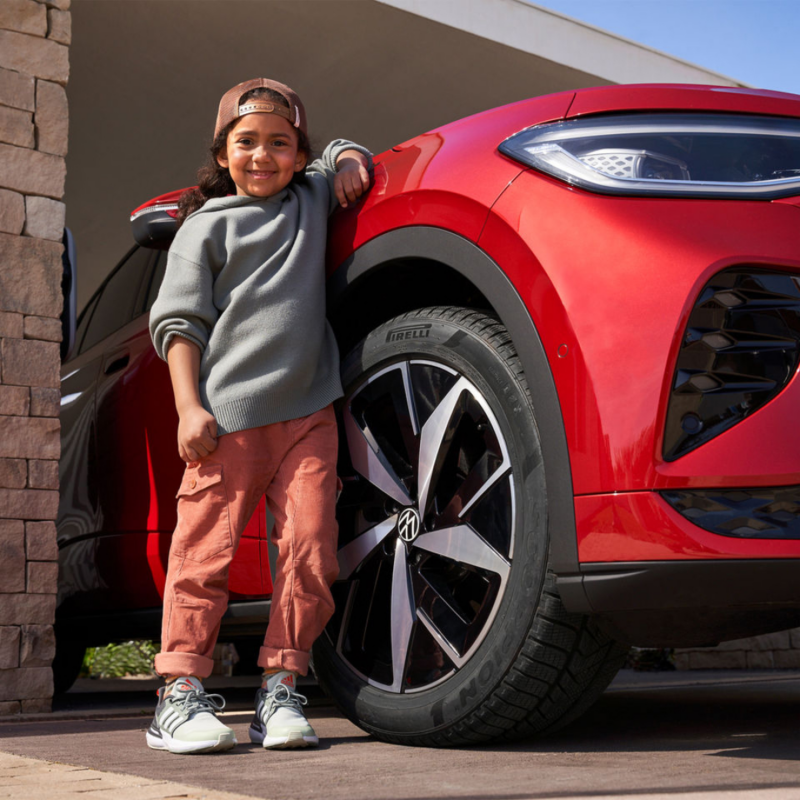 Un niño al lado de un Volkswagen de color rojo