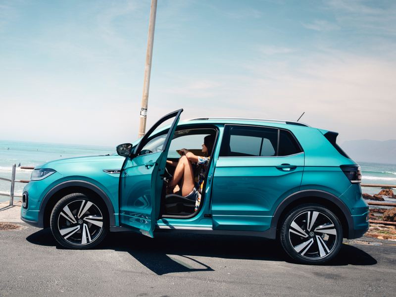 Volkswagen T-Cross esmeralda visto de costado con una chica al volante frente al mar