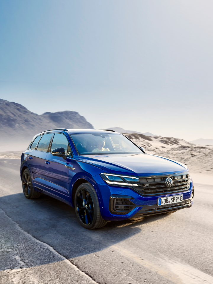 Volkswagen Touareg azul circulando por una carretera de tierra con montañas de fondo.