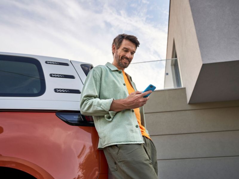 Un hombre con un smartphone apoyado sobre un Volkswagen ID. Buzz