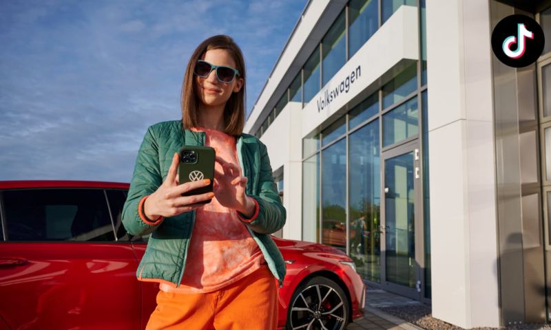 Chica escuchando con un móvil en un concesionario Volkswagen