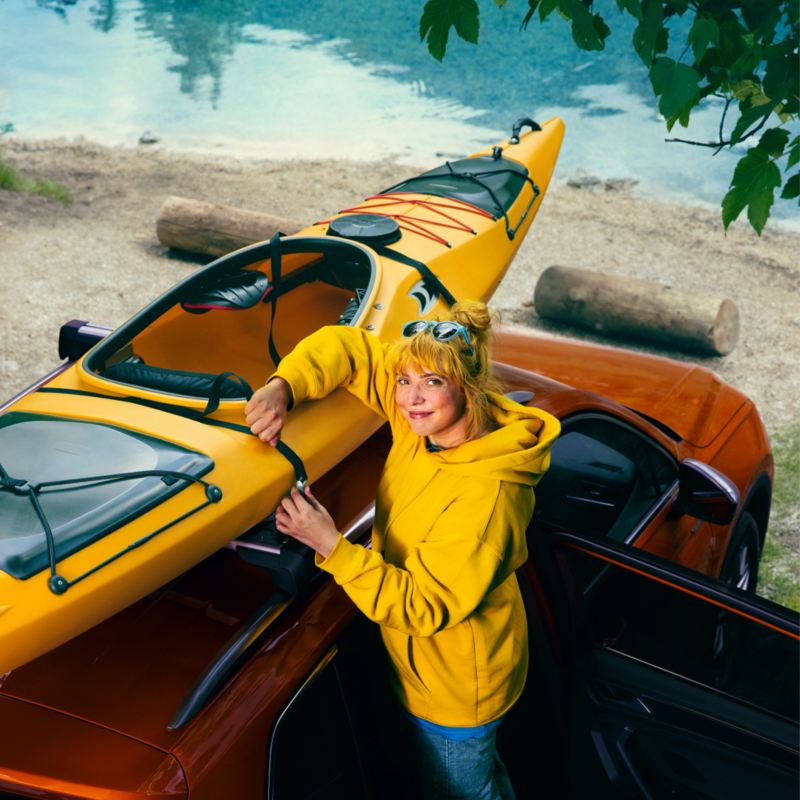 Una chica con sudadera amarilla atando un kayak sobre un SUV Volkswagen