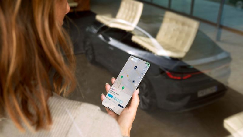 Primer plano de una mujer usando la app de IONITY y un coche en el fondo