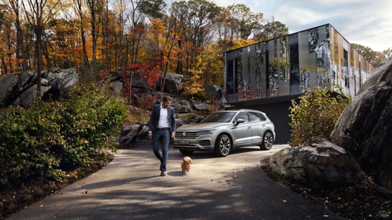 Hombre paseando un perro delante de un Volkswagen Touareg aparcado frente a una casa