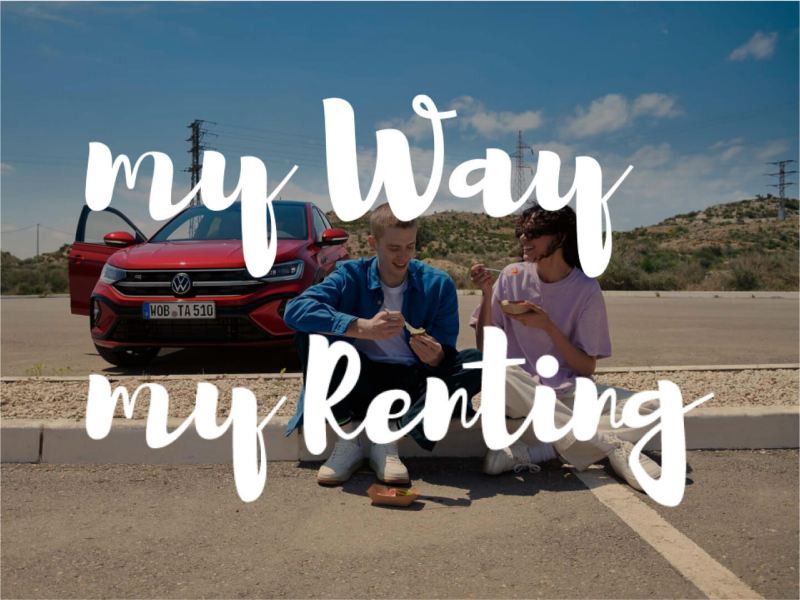 Una pareja sentada en un bordillo delante de un Volkswagen con los logos de My Way y My Renting