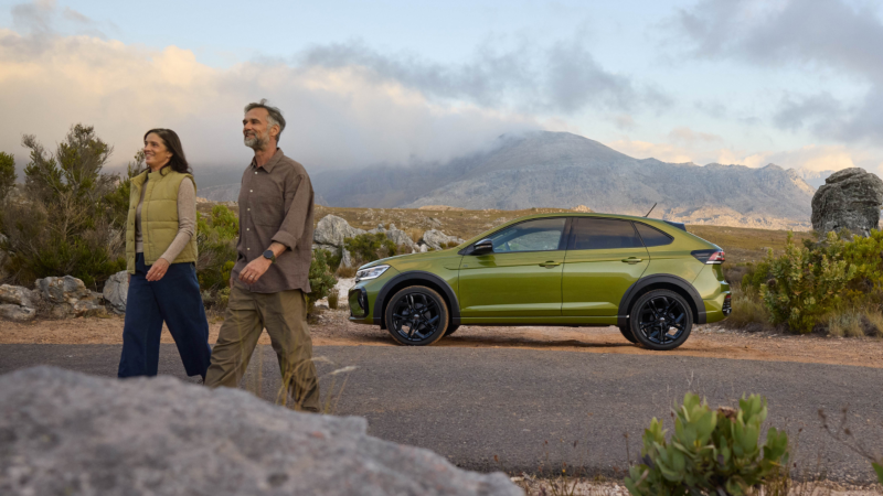 Una pareja delante de un Volkswagen Taigo verde estacionado en una carretera