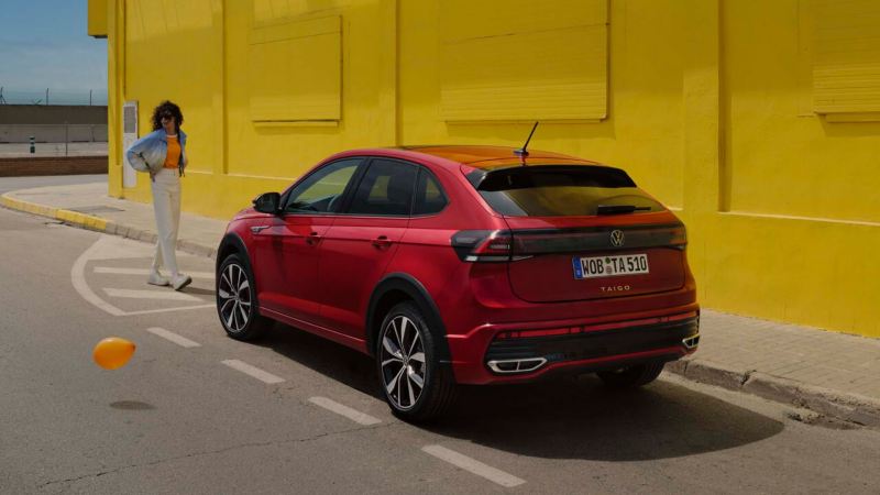 Volkswagen Taigo rojo visto desde atrás y aparcado en la calle frente a un muro amarillo