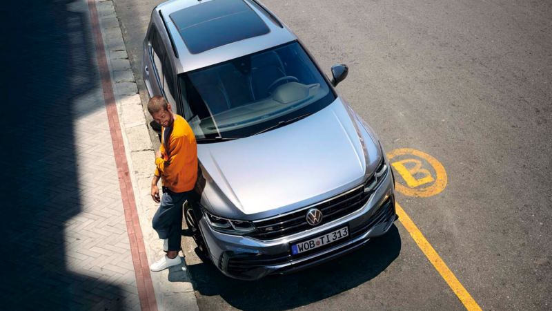 Chico junto a un Volkswagen Tiguan visto desde arriba aparcado en la calle