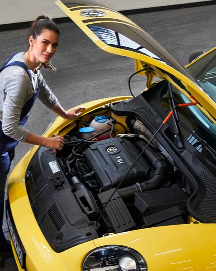 Agente de servicio de Volkswagen verificando el aceite de un Beetle amarillo