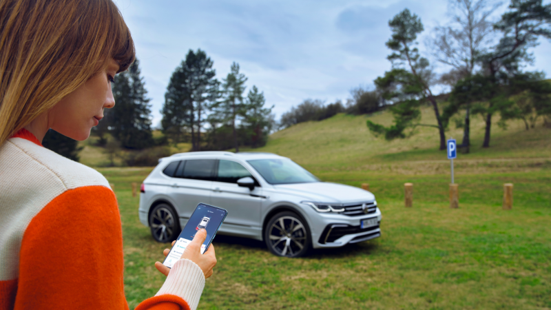 Una chica mirando un móvil delante de un Volkswagen SUV en el campo