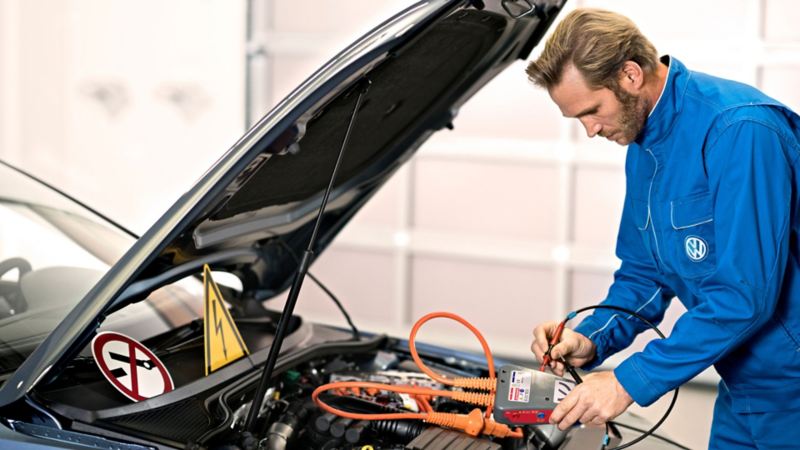 Un mecánico de Volkswagen revisando la batería de un coche con el capó abierto