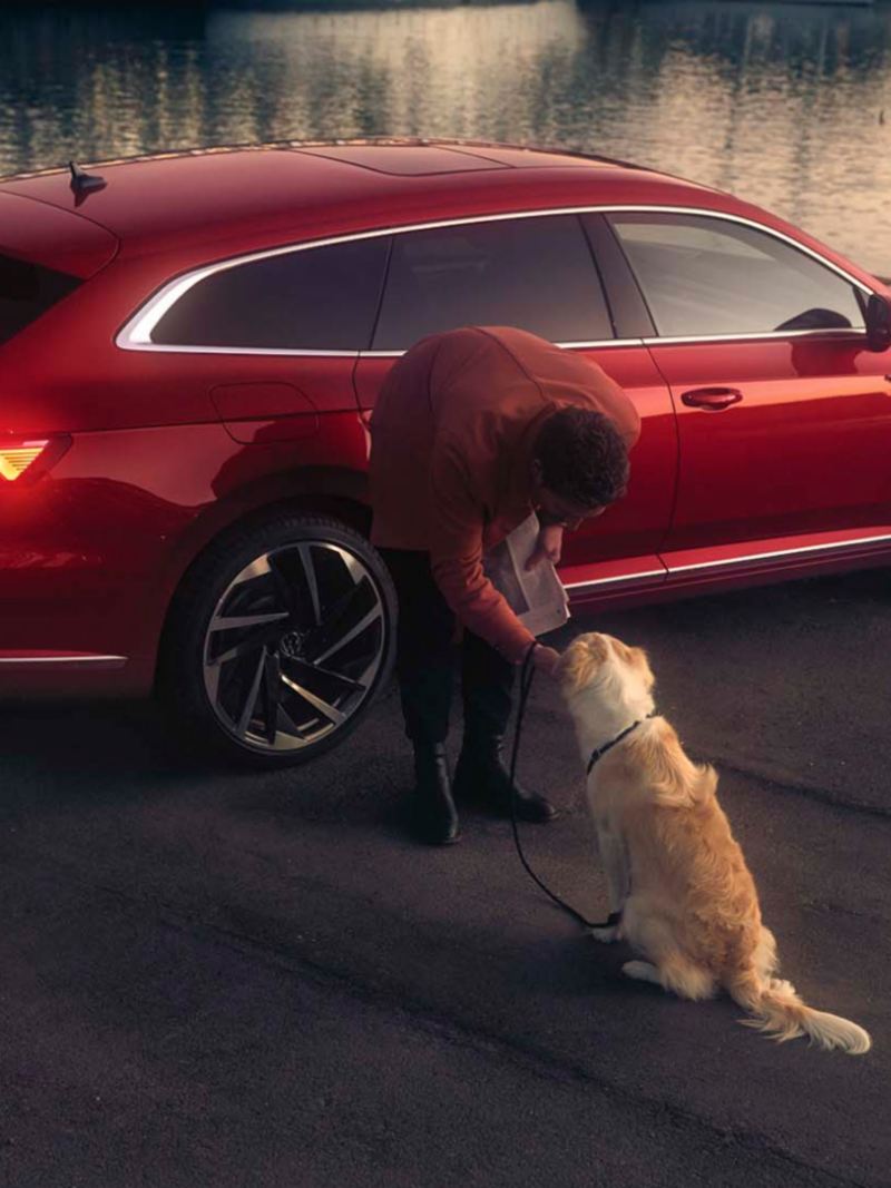 Hombre con su perro dejando a sus espaldas un Arteon Shooting Brake rojo