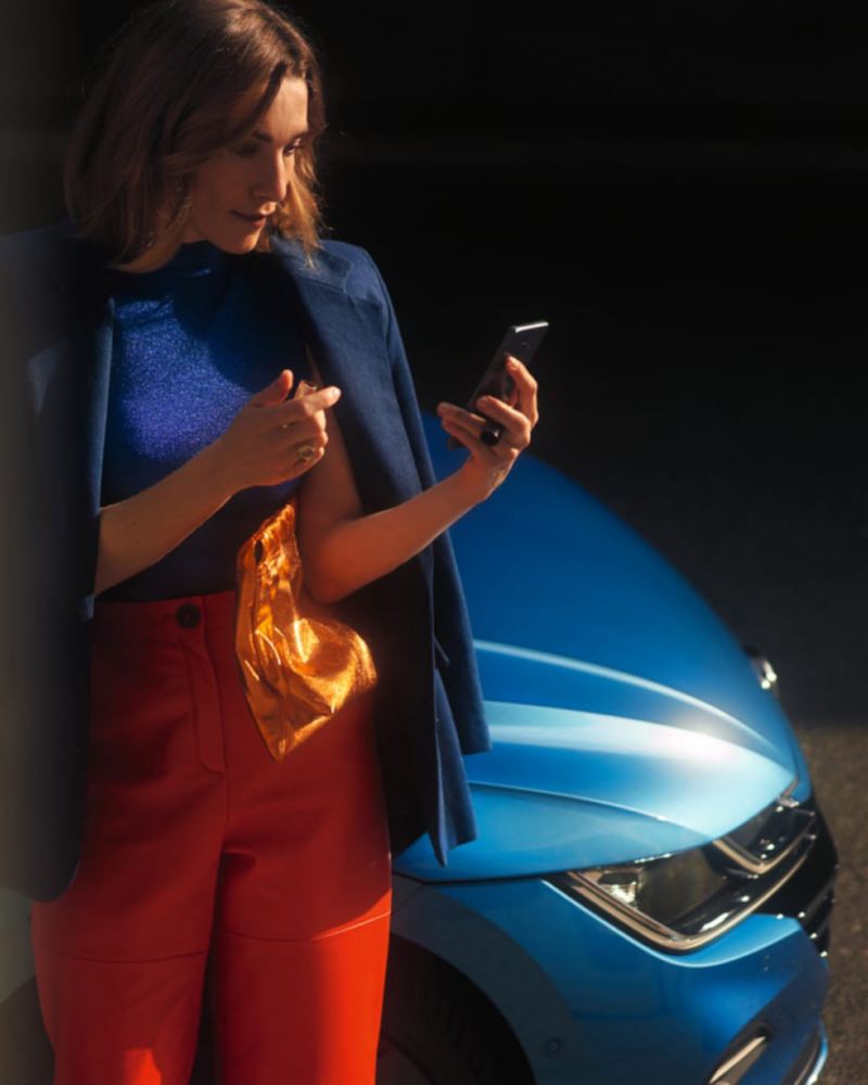 Mujer mirando su móvil de pie delante de un Volkswagen Arteon