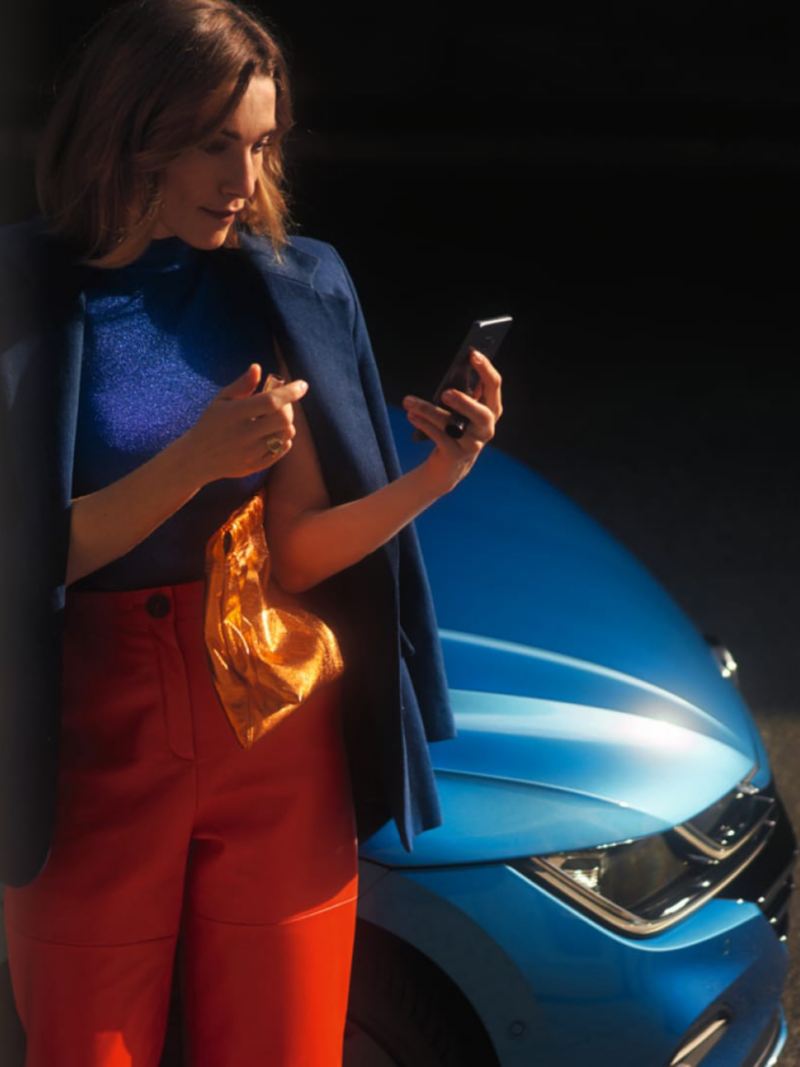 Mujer mirando su móvil de pie delante de un Volkswagen Arteon