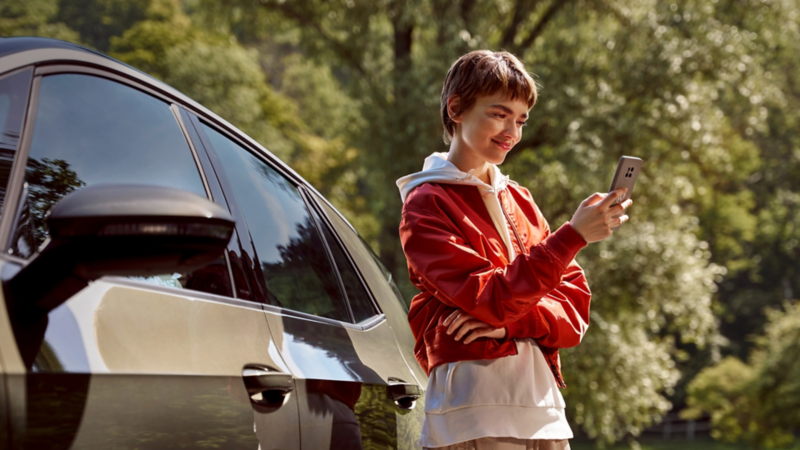 Una chica con un smartphone al lado de un Volkswagen estacionado