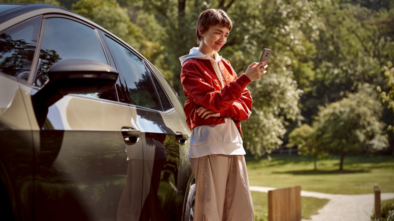 Una chica al lado de un Volkswagen con un smartphone en la mano