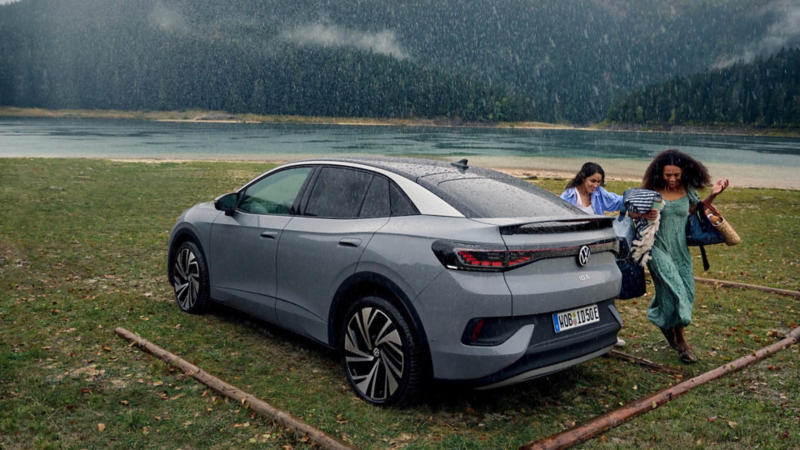 Una mujer y una niña corriendo bajo la lluvia detrás de un Volkswagen ID.4 parado en el campo