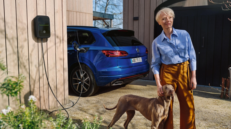 Una mujer junto a un perro al lado de un cargador  de un Volkswagen conectado a carga