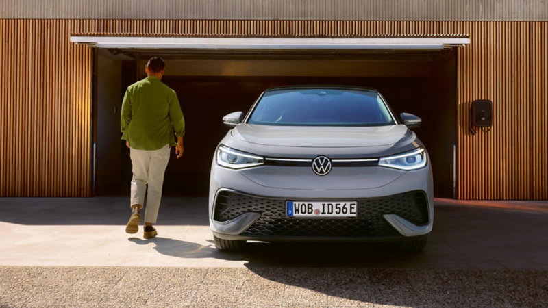 Un hombre junto a un Volkswagen electrico estacionado delante de la puerta de un parking