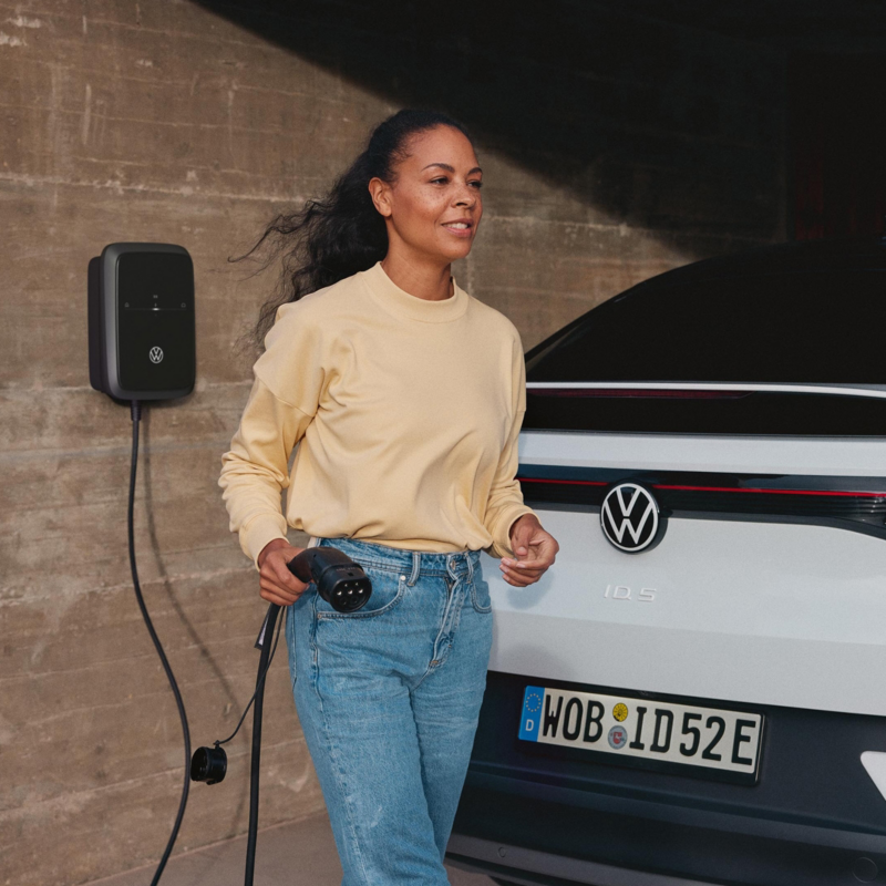 Una mujer agarrando el cable del cargador de un Volkswagen electrico