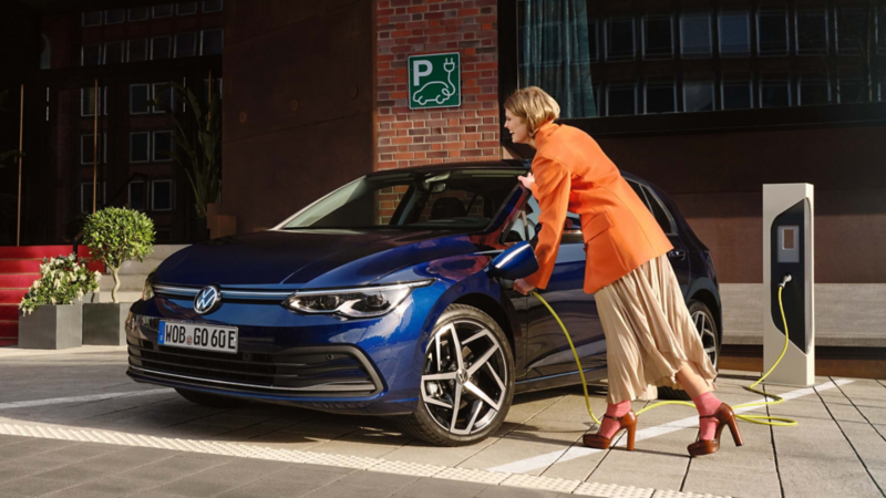 Una chica conectando un Golf azul a una estación de carga en la calle