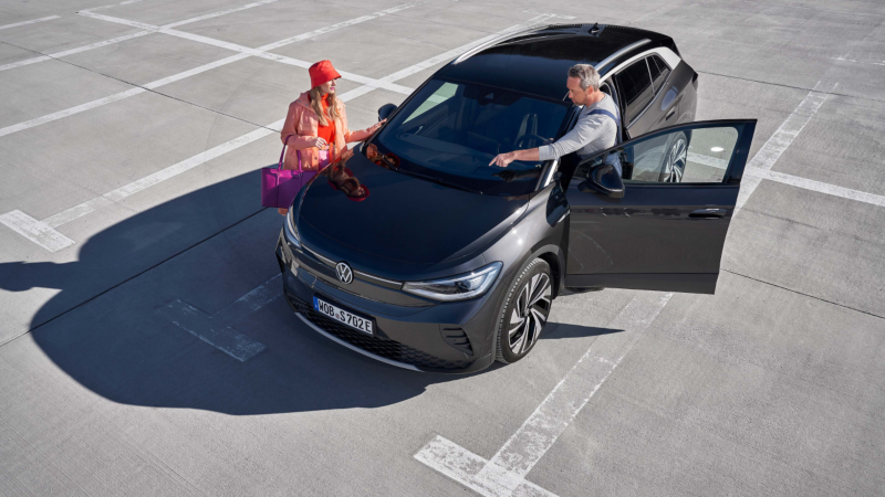 Una mujer y un agente de servicio junto a un Volkswagen ID.4 gris en un parking