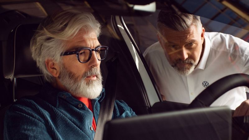 Una hombre al volante de un Volkswagen y un agente de servicio mirando por la ventanilla